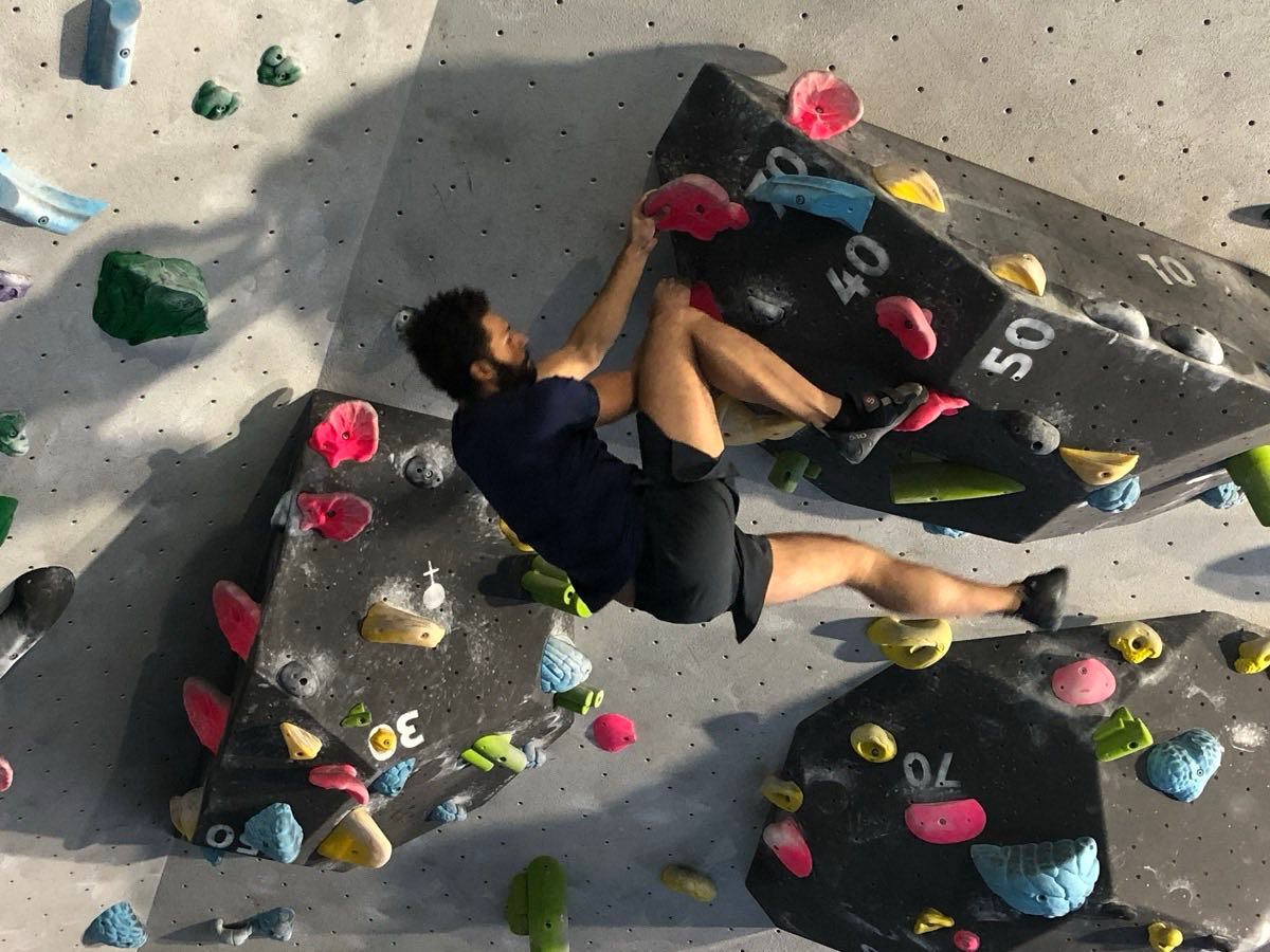 Markus klettert einen Boulder an einer grauen Hallenwand, von oben fotografiert