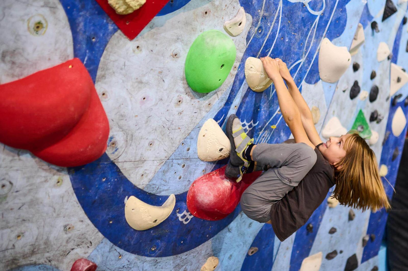 Jugendlicher hängt kopfüber im Überhang an einer bunten Boulderwand